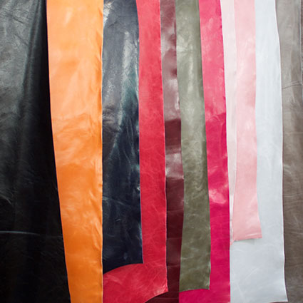 Verschieden farbiges Leder hängt übereinander gelappt auf einer Stange.