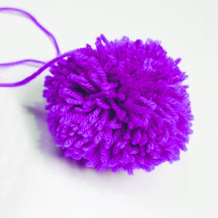 Ein lilafarbener Pompom aus Wolle ist zu sehen.